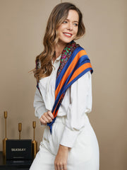 Smiling woman wearing a mulberry silk bohemian square scarf with blue, orange, and paisley patterns.