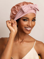 Pink mulberry silk bonnet with bowknot tie, worn by a woman for hair protection.