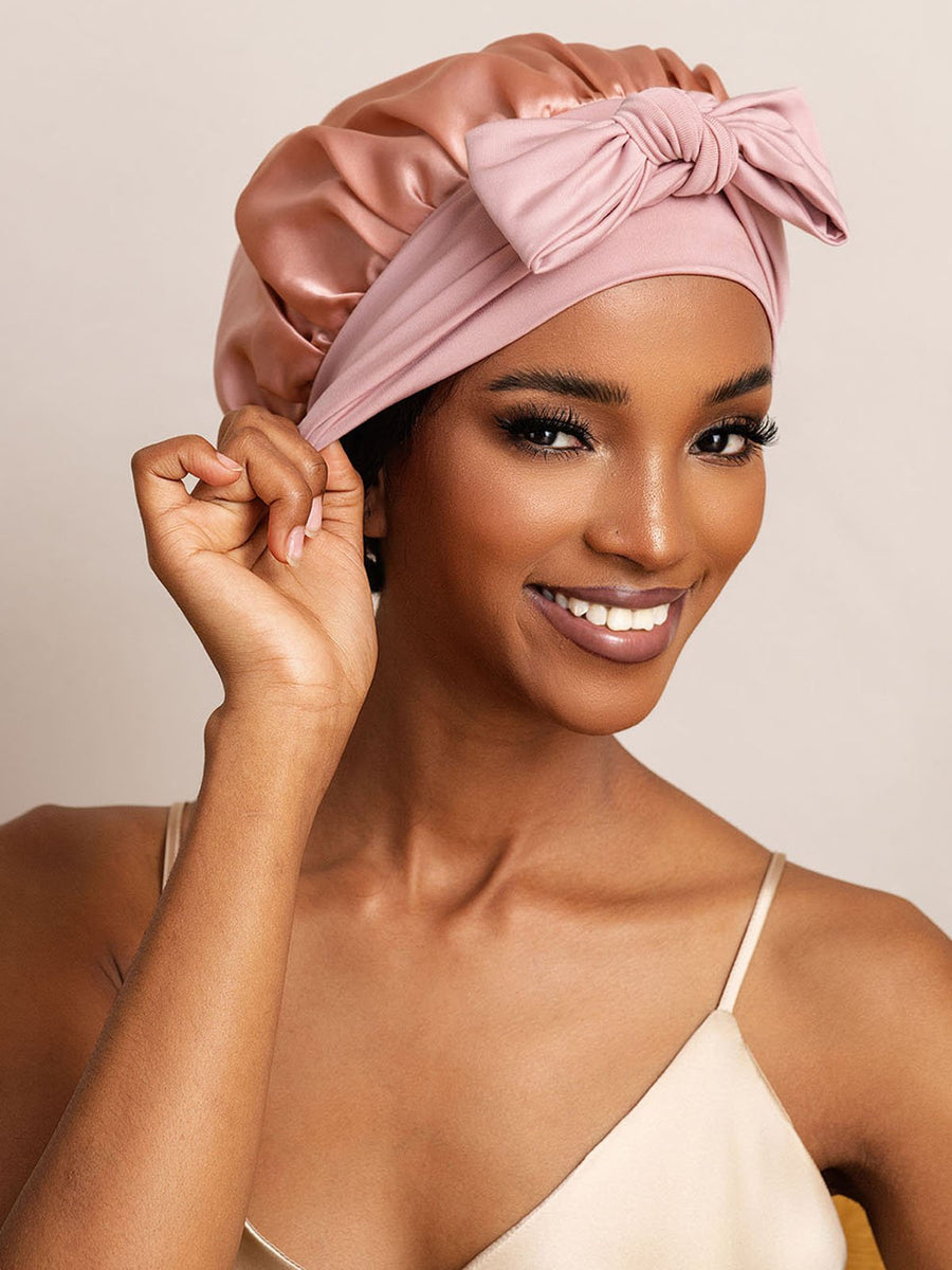 Pink mulberry silk bonnet with bowknot tie, worn by a woman for hair protection.