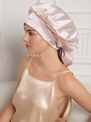 Pink mulberry silk casual bonnet with long ribbons, worn by a woman in a matching silk top.