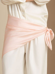 Elegant pink mulberry silk scarf tied around a waist, complementing a white silk shirt and pants.