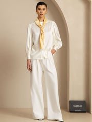 Elegant woman in white silk top and pants, accessorized with a yellow mulberry silk scarf.