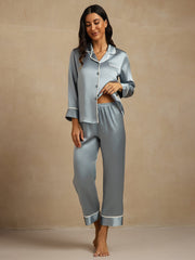Women's grayish blue mulberry silk pajama set with white contrast piping, long sleeves, and button-front top.