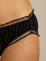 Black mulberry silk panty with sheer ruffle trim, shown on a woman's hip.