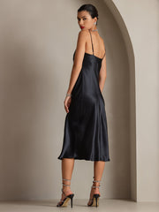 Black 100% mulberry silk cowl neck midi dress on a woman, showcasing its elegant drape and spaghetti straps.
