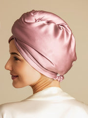 Woman wearing a pink mulberry silk hair towel wrap, twisted and secured, over a cream silk top.