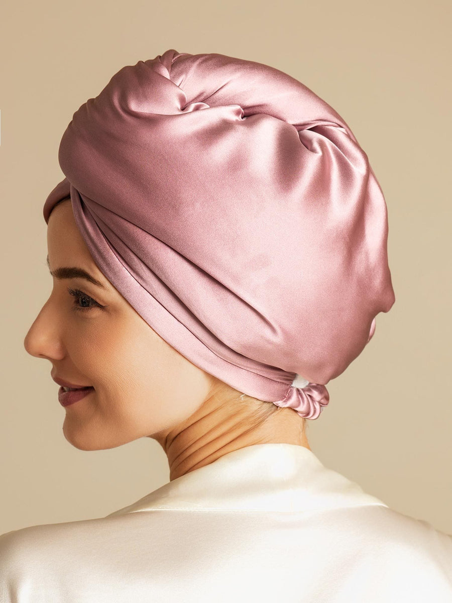 Woman wearing a pink mulberry silk hair towel wrap, twisted and secured, over a cream silk top.