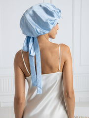 Light blue mulberry silk bonnet with long ribbons, worn by a woman in a white silk nightgown.