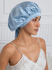 Elegant light blue mulberry silk bonnet with long ribbons, worn by a woman over a white lace top.