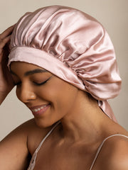 Elegant mulberry silk bonnet in blush pink, worn by a smiling woman.