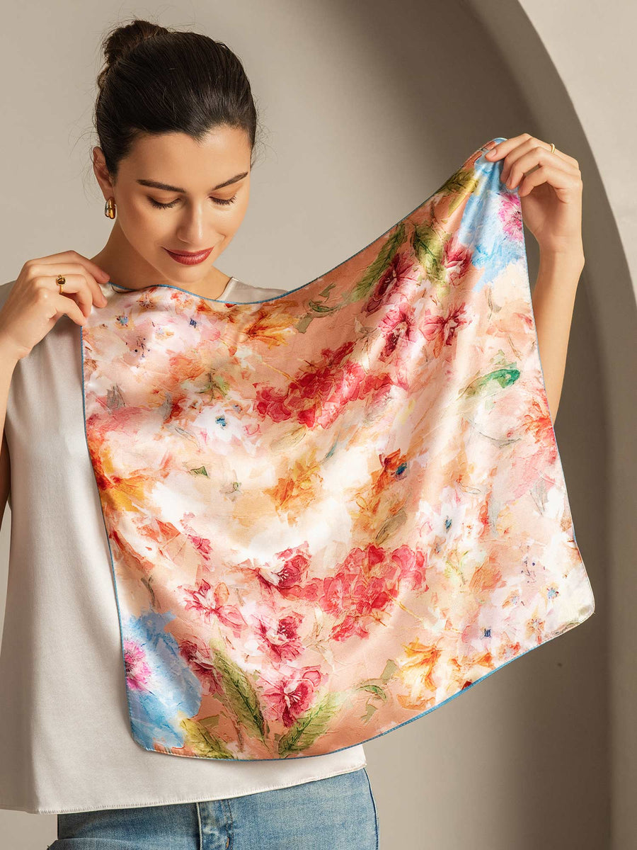 Woman holding a 53x53cm 100% mulberry silk floral bliss square scarf with vibrant pink, orange, and blue hues.