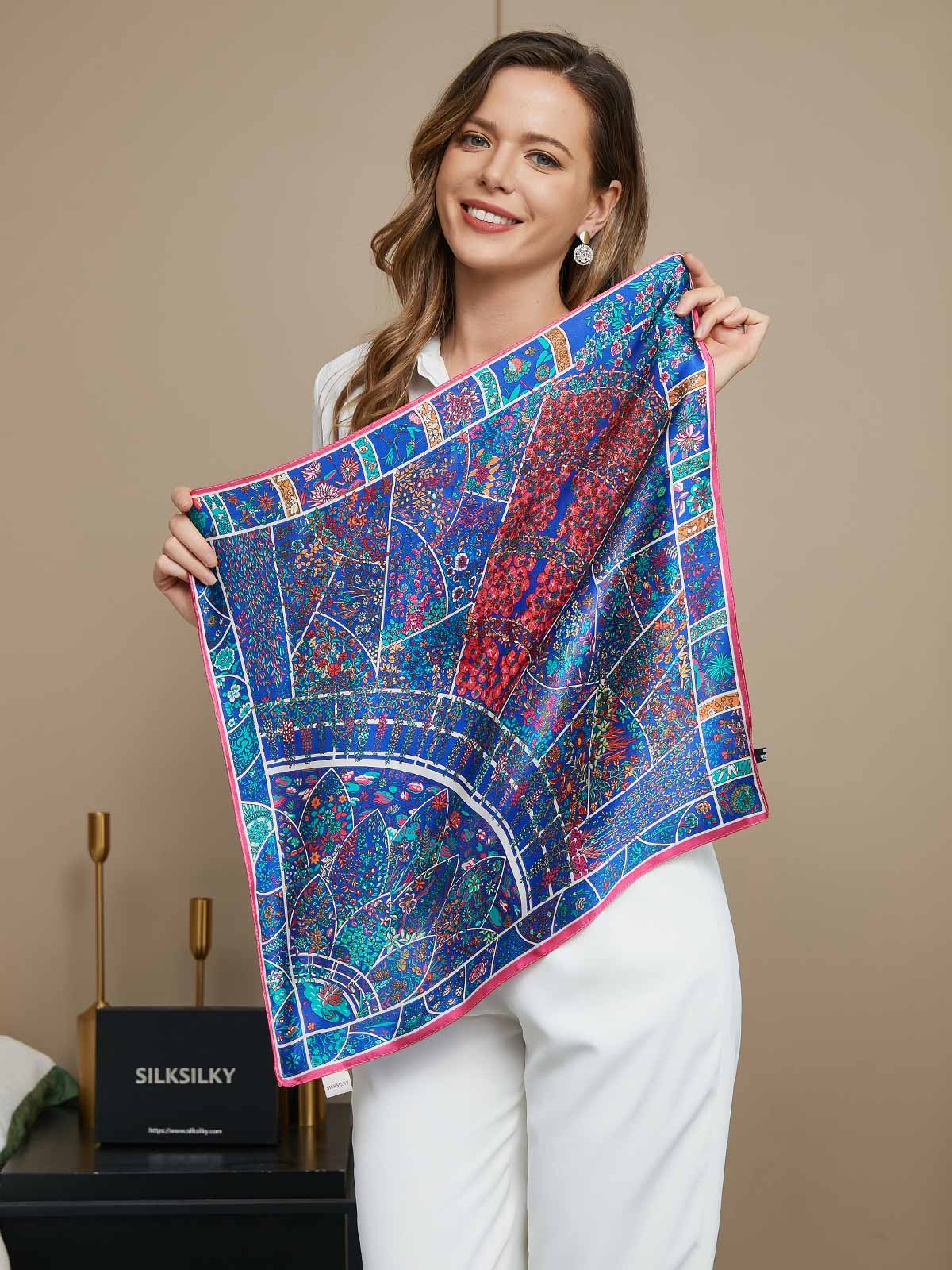 Woman holding a blue mulberry silk floral pattern scarf with pink trim, 53x53cm.