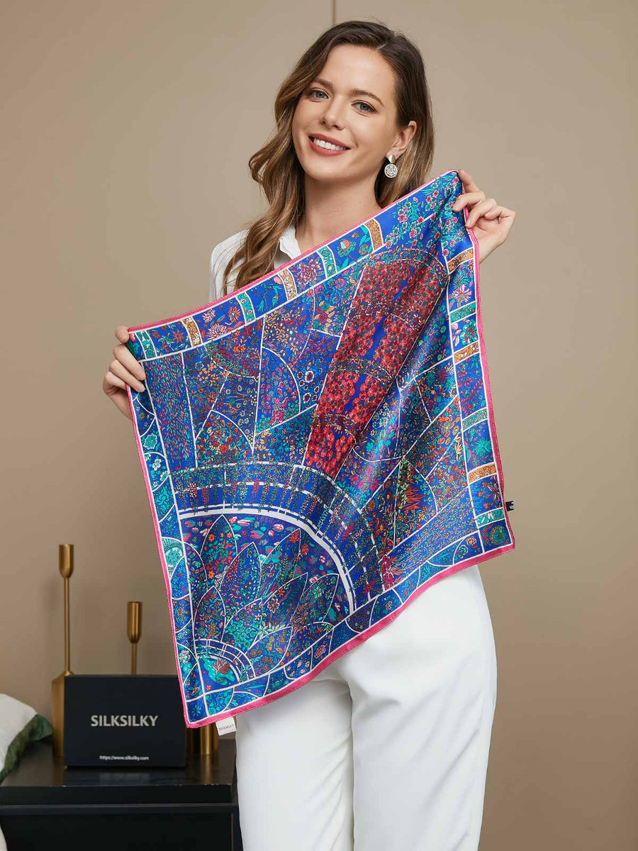 Woman holding a blue mulberry silk floral pattern scarf with pink trim, 53x53cm.