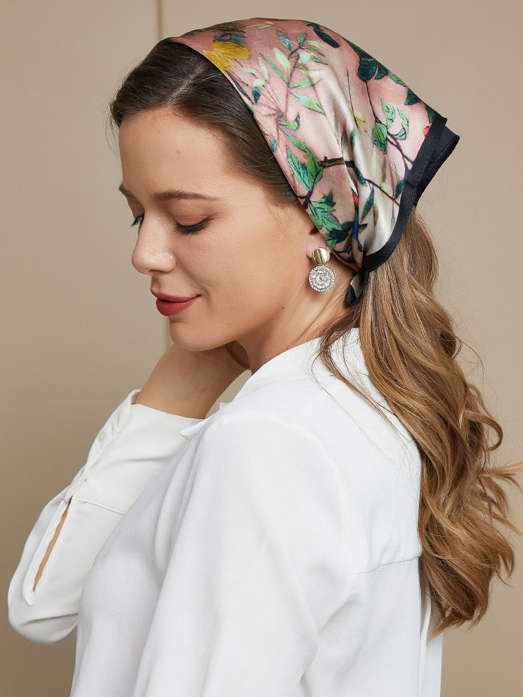 Woman wearing a 53x53cm mulberry silk floral pattern square scarf in soft pink and green tones.