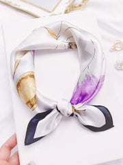 White mulberry silk floral printed square scarf with purple, gold, and black accents, tied in a knot.