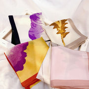 Four folded 100% Mulberry silk floral printed square scarves in purple, yellow, brown, and pink.