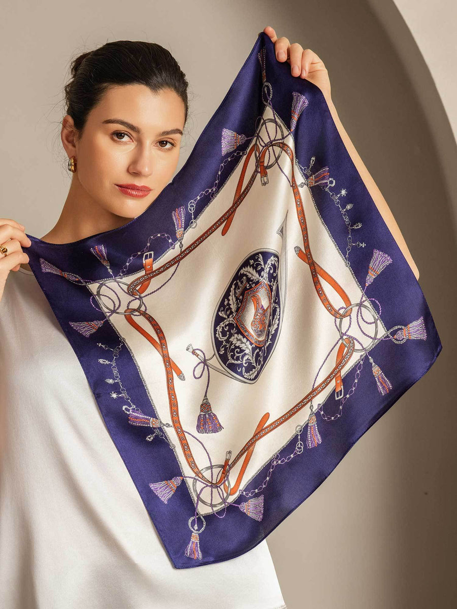 Woman holding a mulberry silk floral square scarf with a navy blue and white equestrian pattern.