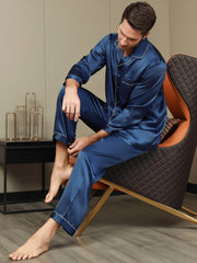 Men's navy blue mulberry silk long sleeve pajama set with white piping, worn by a man sitting.