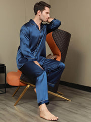 Men's navy blue mulberry silk long sleeve pajama set with white piping, shown on a seated man.