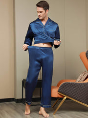 Men's navy blue mulberry silk long sleeve pajama set with white piping, modeled indoors.