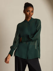 Dark green 100% Mulberry silk long sleeve sheer blouse with split hem, worn by a woman.
