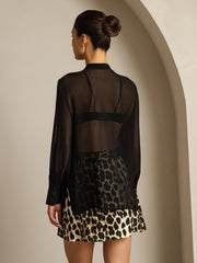 Woman in black sheer mulberry silk long sleeve blouse over leopard print skirt.