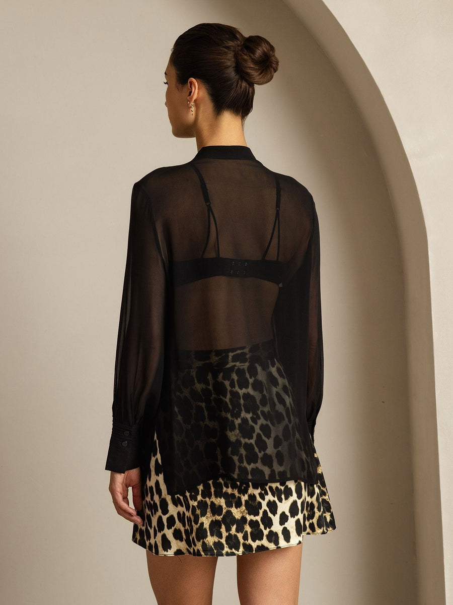 Woman in black sheer mulberry silk long sleeve blouse over leopard print skirt.