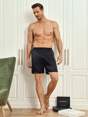 Man in black mulberry silk lounge shorts, standing by white closet.
