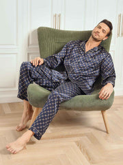 Men's navy mulberry silk pajamas with gold chain print, long sleeves, and pants, worn by a man in a chair.
