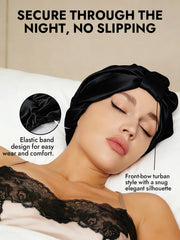 Black mulberry silk night turban bonnet with front-bow design and elastic band, worn by a woman sleeping.