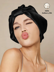 Black 100% Mulberry Silk Night Turban Bonnet on a woman, winking and blowing a kiss.