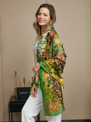 Woman wearing a vibrant mulberry silk scarf with an oil painting pattern, green border, and white top.