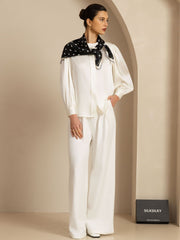 Model wears a white silk blouse and trousers, accessorized with a black mulberry silk paw print square scarf.