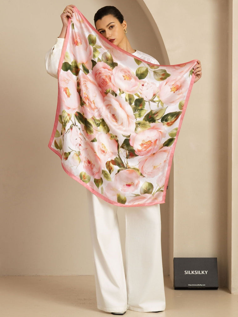 Woman holding a pink floral print mulberry silk scarf (90x90cm) with a pink border.