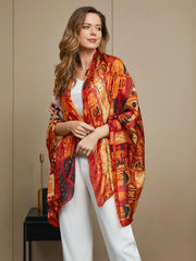 Woman wearing a vibrant orange and red abstract print mulberry silk scarf/shawl, draped over white top and pants.