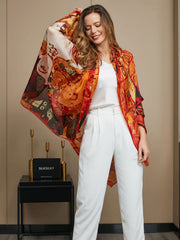 Women's mulberry silk scarf with vibrant red and orange abstract print, draped over a white outfit.