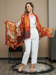 Woman wearing a large 100% mulberry silk printed rectangle scarf in warm orange and red tones.