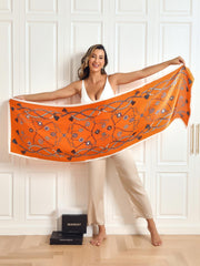 Woman holding a vibrant orange mulberry silk scarf with a silver chain and floral print.