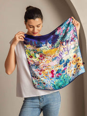 Woman holding a vibrant mulberry silk square scarf with a colorful floral garden print.