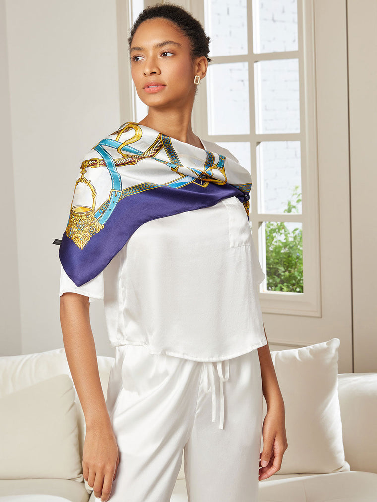 Woman wearing a white 100% Mulberry silk pajama set and a printed square silk scarf with gold and blue chain pattern.