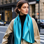 Woman wearing a vibrant blue 100% Mulberry silk rectangle scarf with a beige coat and black turtleneck.