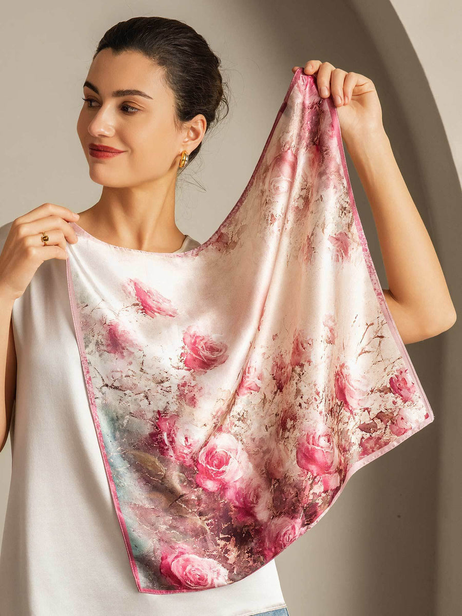 Woman holding a 100% mulberry silk square scarf with a delicate pink rose pattern, 53x53cm.
