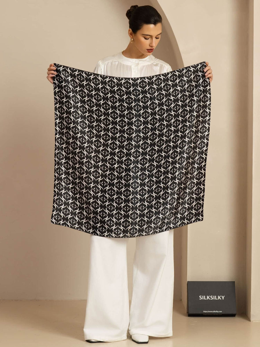 Woman holding a black and white patterned 90x90cm mulberry silk square scarf.