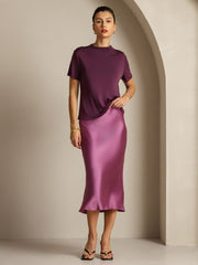 Women's mulberry silk short sleeve mock t-shirt in deep plum, paired with a satin midi skirt.