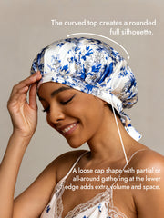 Women's white and blue floral mulberry silk sleep bonnet with ribbons, worn by a smiling woman.