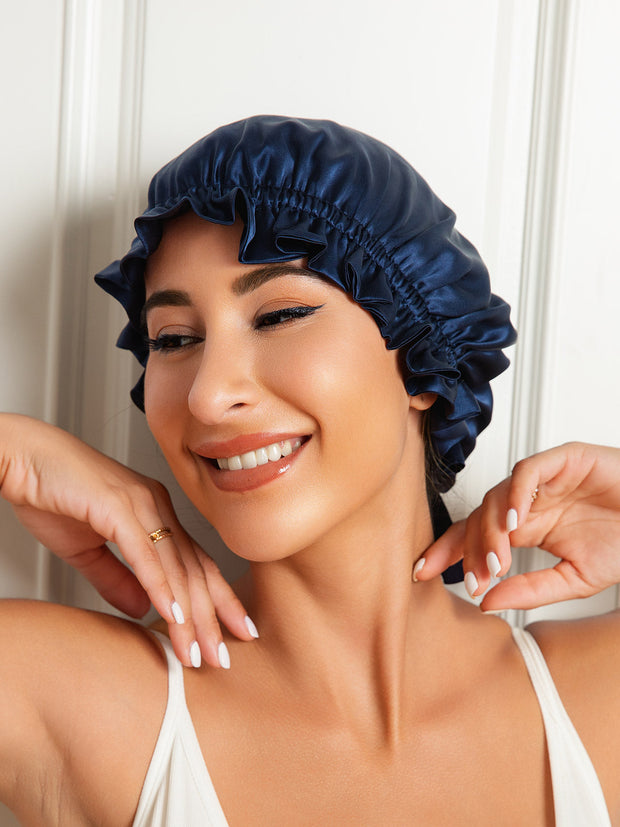 Smiling woman wearing a navy blue mulberry silk sleep cap with a ruffled edge and ribbon tie.