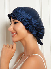 Navy blue mulberry silk sleep cap with a ruffled edge and ribbon tie, worn by a smiling woman.