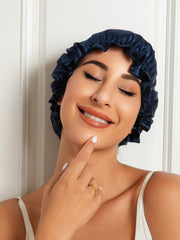 Smiling woman wearing a navy blue double-layer mulberry silk sleep cap bonnet with a ruffled edge.