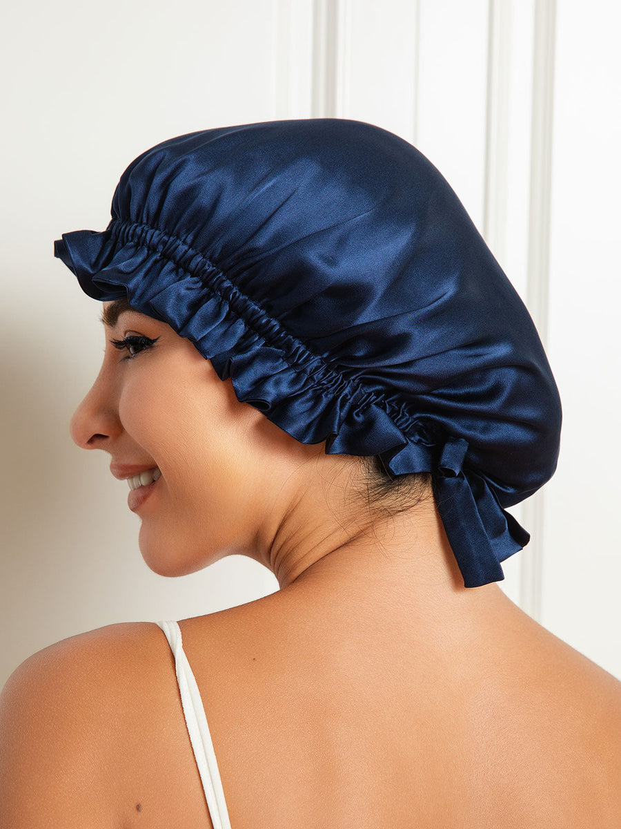 Navy blue mulberry silk sleep cap with a ruffled edge and ribbon tie, worn by a woman.