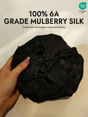 Black double-layer mulberry silk sleep cap bonnet held in hand, showing smooth fabric and elastic band.